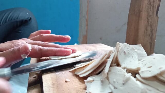 Slicing raw Indonesian meatball horizontally with a knife on wooden board