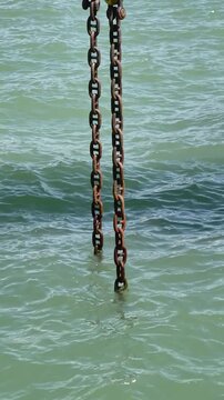Rusty metal chain hanging into sea water at harbor. Marine industry and port infrastructure concept.