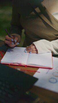 Close-up of a business professional's hands writing notes in a red notebook. This portrays focused work and planning during an outdoor business meeting