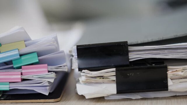 Stack of business documents with colorful binder clips on office desk, representing paperwork organization, file management, corporate administration, audit records, and workflow productivity.