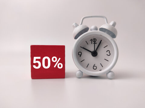 A red wooden block printed with white 50% text stands next to a small white twin bell alarm clock