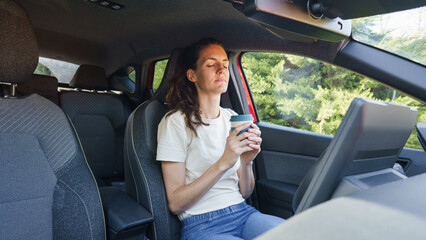 Naklejka premium Woman relaxing in car enjoying coffee break with eyes closed