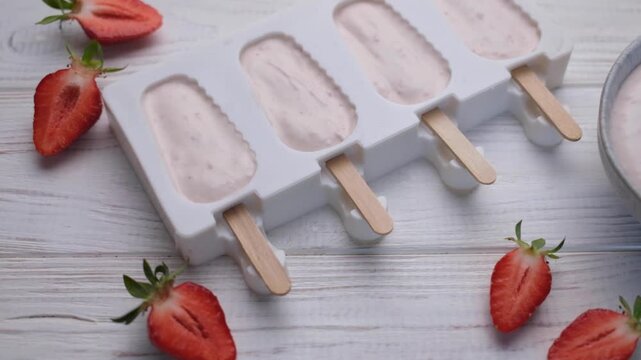 Preparing homemade strawberry yogurt popsicles on a table