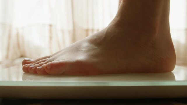 Close-up of feet stepping onto a digital bathroom scale for weighing. Concept of weight control, health monitoring, fitness goals, body care, and healthy lifestyle at home. High quality 4k footage