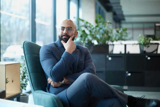 A man in a suit is sitting in a chair in front of a laptop