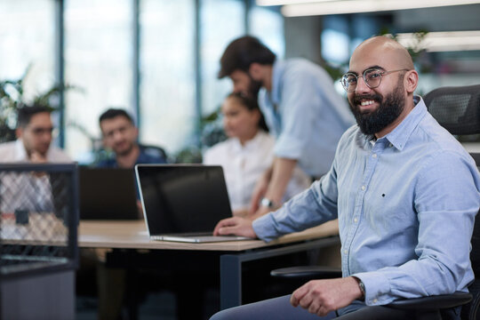 A man in a blue shirt is sitting at a desk with a laptop