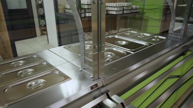 Stainless food containers with lids on glass display of modern school canteen. Sterile equipment for cooked products keeping in cafeteria