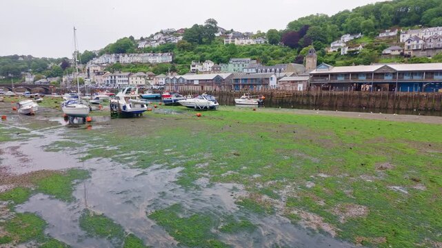 Authentic coastal video footage showing East Looe Harbour in Cornwall, England. Slow panoramic movement from Looe Bridge across the waterfront towards the harbour entrance and sea on a wet, overcast 