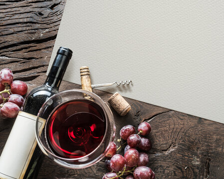 Top view still life of red wine bottle, glass of red wine, and fresh grapes on a rustic wooden table.