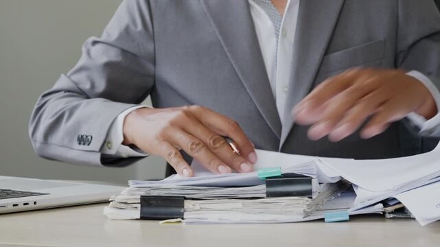 Business employee handling large paperwork folders with black binder clips, symbolizing administrative duties, records review, audit preparation, deadline pressure, and office workload.