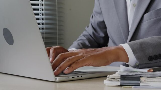 Close up of office employee entering data on laptop with documents nearby, showing administrative processing, digital records, file management, business communication, and workflow control.