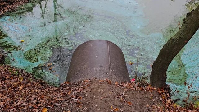 Industrial pipe discharging toxic waste into polluted river with chemical film closeup