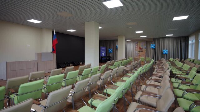Russian national flag near podium in empty school event hall. Rows of cozy seats prepared for visitors in large school auditorium