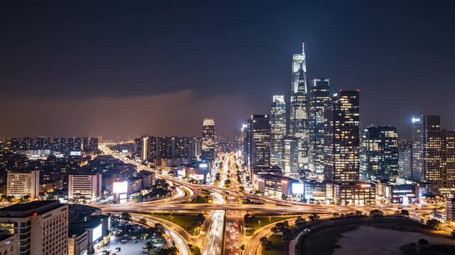 Illuminated cityscape stretches across the horizon at dusk, showcasing a vibrant urban sprawl of towering skyscrapers and expansive illuminated expressways pulsing with vehicular motion under