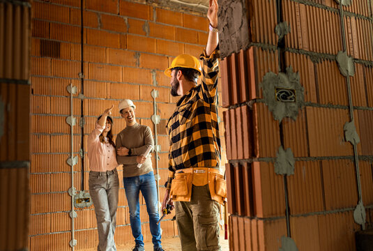 Construction worker showing the progress of a house build to an adult couple at the construction site.