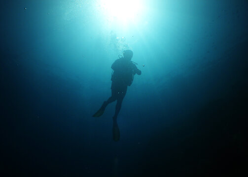Scuba diver silhouette ascending toward dramatic sunburst in deep blue ocean