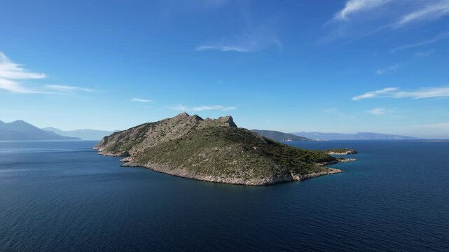 Aerial panorama of uninhabited Moni island near Aegina Greece. Steep cliffs, green pine trees, and hills under a clear blue sky.