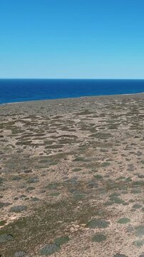 Vertical drone shot sliding backward along the Bunda Cliffs above the sparse outback with blue ocean and sky in Australia