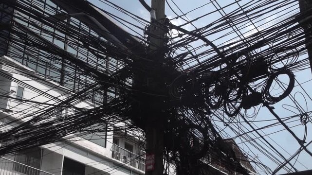 Messy power wires are tangled on the electrical pole, creating a chaotic arrangement of internet cables and powerlines in Thailand.