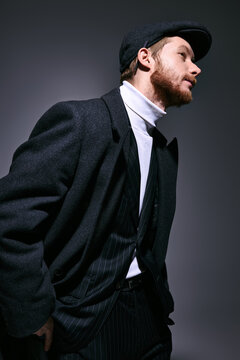 Stylish red haired man in fashionable attire poses confidently against a moody backdrop.