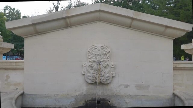  Stone fountain with carved bearded face relief pouring thin water stream.