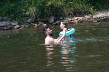 Fototapeta premium A father and daughter enjoy a playful moment in a river, the girl using an inflatable ring.