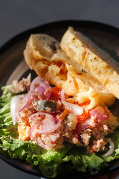 Delicious slices of soft sourdough bread served alongside a vibrant tuna salad, mixed with sliced red onions, fresh lettuce, and tangy pickled vegetables on a dark plate.