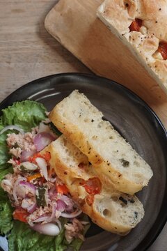 Delicious slices of soft sourdough bread served alongside a vibrant tuna salad, mixed with sliced red onions, fresh lettuce, and tangy pickled vegetables on a dark plate.
