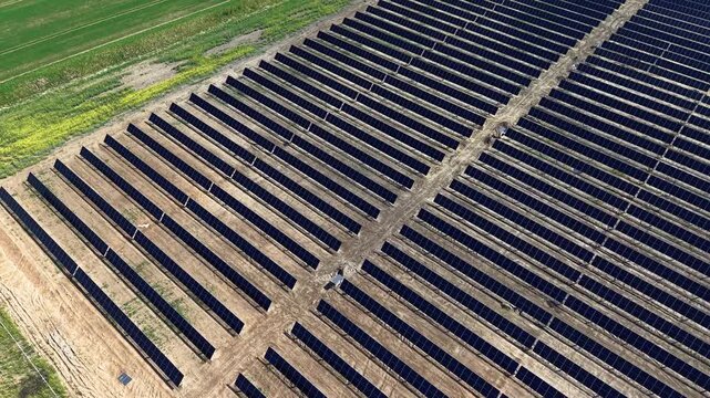 Drone footage captures rows of solar panels across a vast energy farm under clear skies, showcasing clean technology, sustainable power generation, and geometric patterns in sunlight.