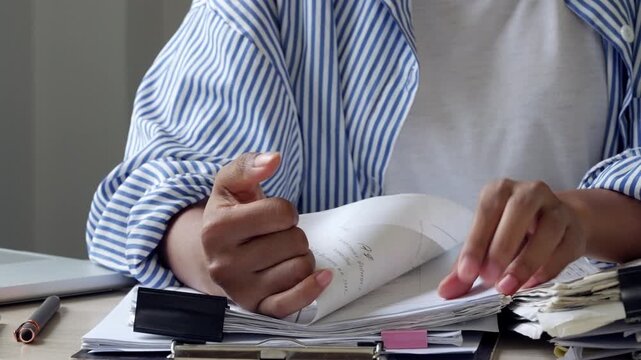 Female employee sorting thick office documents in a modern workplace, representing paperwork overload, busy administration, deadline pressure, corporate workflow, file review, and document control.