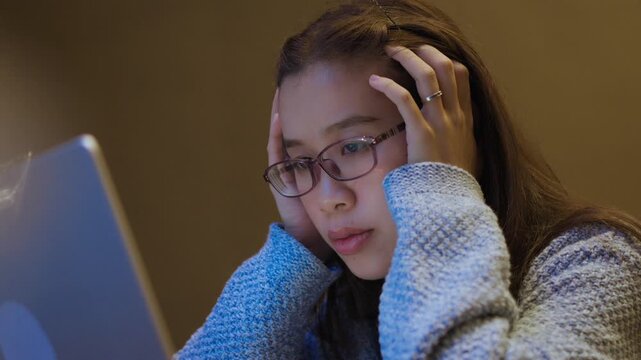 Tired Young Woman Resting Chin While Working on Laptop at Night.  Work fatigue, office stress, burnout, remote work pressure, tired employee