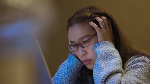 Tired Young Woman Resting Chin While Working on Laptop at Night.  Work fatigue, office stress, burnout, remote work pressure, tired employee