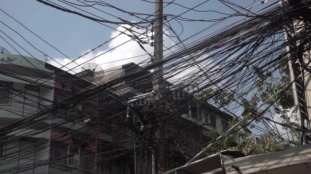 Messy power wires are tangled on the electrical pole, creating a chaotic arrangement of internet cables and powerlines in Thailand.