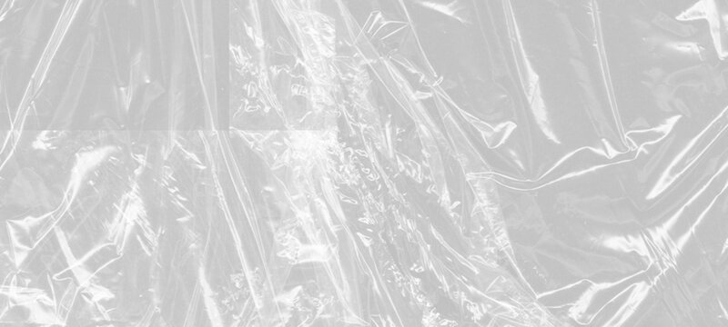 Overhead shot of creased transparent plastic sheeting with visible texture from fine lines and uneven surfaces, abstract light and shadow play.