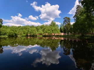 Obraz premium Calm lake water reflecting bright white clouds and lush green trees under a sunny blue sky