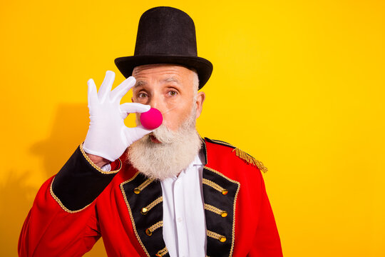 Circus ringmaster with pink clown nose performs a trick in festive show on bright yellow background