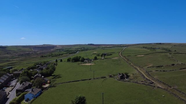 Panoramic aerial drone view of the village of Blackshaw head in Calderdale West Yorkshire with Higher Back lane surrounded by fields in summer sunlight