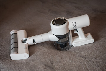 Side view of a modern white cordless vacuum cleaner with motorized floor brush resting on a soft grey carpet, portable handheld device for home cleaning. © Serhii
