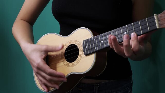 Woman playing a wooden ukulele against a teal background