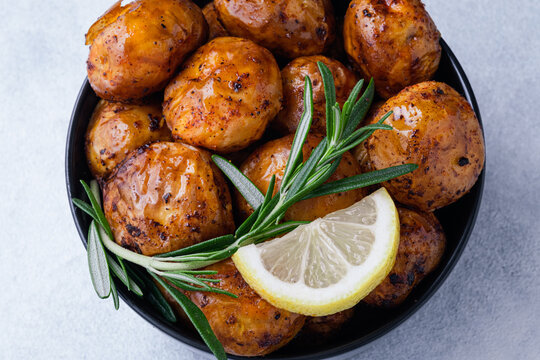A bowl holds roasted crispy potatoes garnished with lemon slices and fresh rosemary on a blue background. Homemade comfort food and healthy side dishes. top view