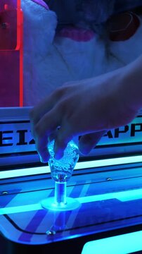  Hand on the joystick of a claw machine with plush toys under neon lights