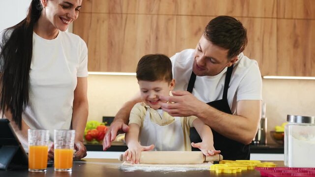 Family engages in cooking activity in a modern kitchen, with parents assisting young boy who is playing with dough on the countertop