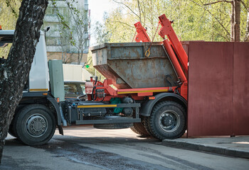 Garbage truck loads metal container with household and construction waste. Concept of waste disposal, utilities, ecology. Not AI. © Olga