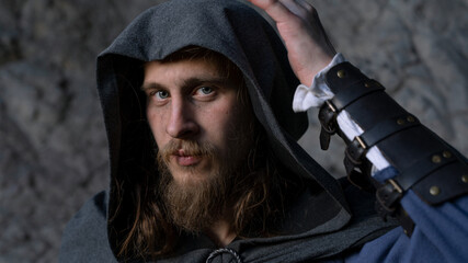 Fototapeta premium Intense gaze of a bearded man with hood and leather bracers against textured stone backdrop.