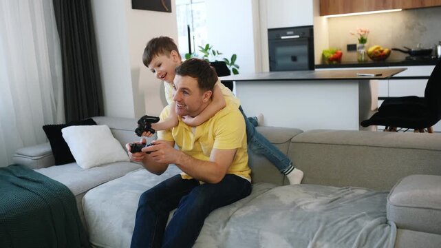 Caucasian father and son celebrating together on a sofa, both wearing matching yellow shirts, holding a video game controller in a modern living room setting