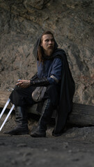 Fototapeta premium A weary warrior with a sword rests against a log, gazing thoughtfully into the distance.