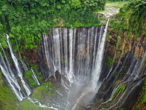 Drone view of Tumpak Sewu Waterfall cascading through a steep canyon surrounded by dense tropical vegetation in East Java, Indonesia.