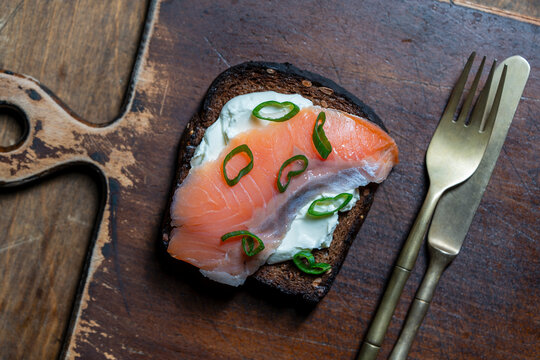 Smoked salmon toast with cream cheese and chives on wooden board. Top view of gourmet open sandwich with salmon red fish slice cream cheese and green onions on a rustic cutting board