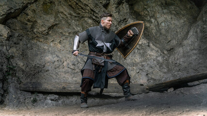 A knight stands ready with sword and shield amidst a rocky landscape. © horimono