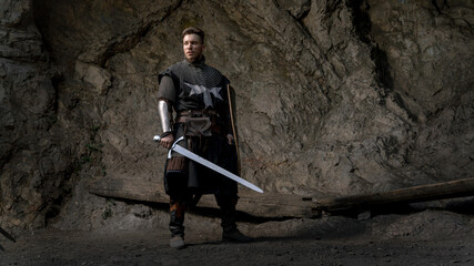 A stoic knight stands ready with sword and shield amidst a rugged, rocky landscape. © horimono